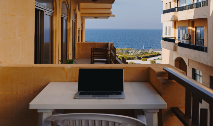 Laptop na stoliku przed balkonem podczas pracy zdalnej.